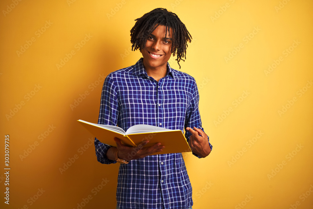 Afro american student man with dreadlocks reading book over isolated yellow background very happy pointing with hand and finger Afro american student man with dreadlocks reading book over isolated yellow background very happy pointing with hand and finger