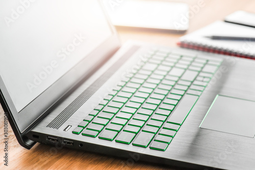 Desk laptop or modern computer with blank screen on rustic table. Spiral notepad placed on wooden desktop with pen and backlight. Business notebook detail concept.