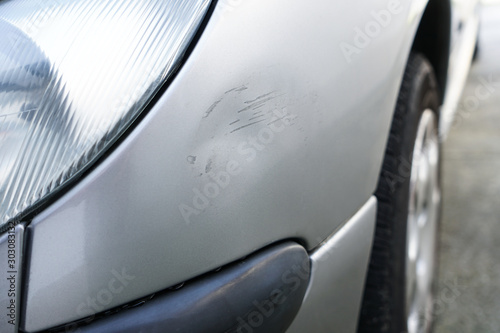 Close up of dent and scratches on side of old silver gray car. Damage from crash accident, parking lot or traffic.