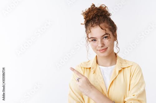 Charming friendly helpful redhead curly messy bun hairstyle and freckles female student show way pointing left smiling pleasantly directing advertisement, giving instuctions how get place photo