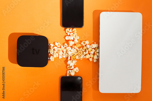 Remote control devices concept. Set of controller and micro console for TV watching and online streaming. Popcorn and snacks on the orange background. Top view. Space for a text. Close up. photo