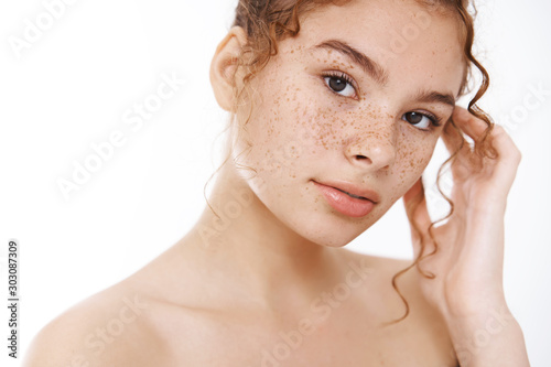 Beauty, skincare concept. Tender redhead young woman naked freckles look camera sensually gently touching pure clean unaltered facial skin applying daily treatment cosmetology products after shower