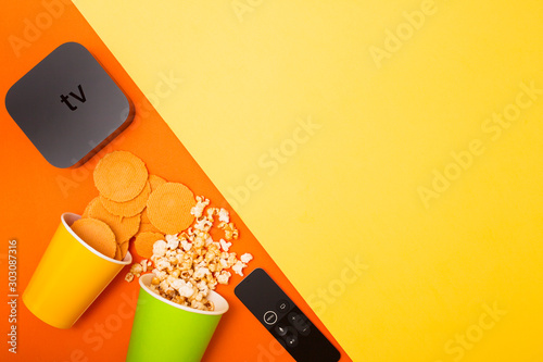 Remote control devices concept. Set of controller and micro console for TV watching and online streaming. Popcorn and snacks on the yellow background. Top view. Space for a text. Close up. photo