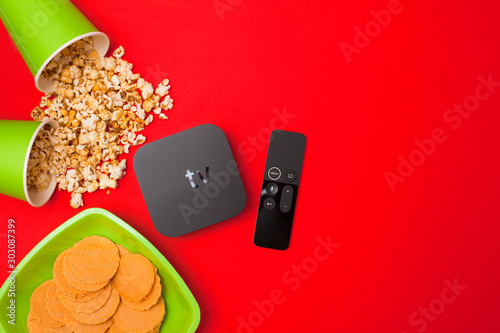 Remote control devices concept. Set of controller and micro console for TV watching and online streaming. Popcorn and snacks on the red background. Top view. Space for a text. Close up.