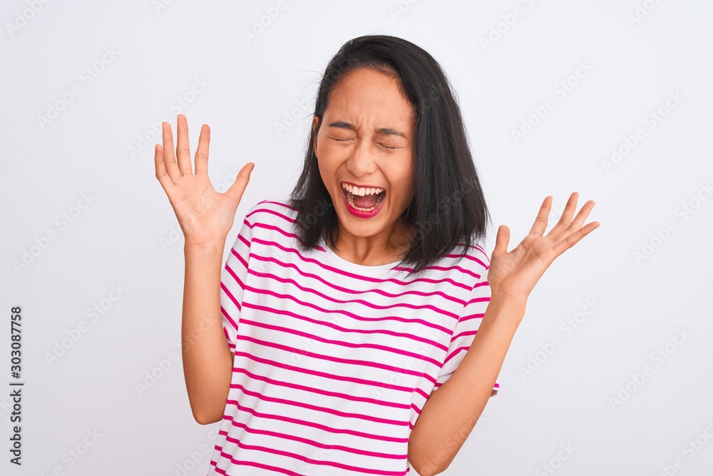 Young chinese woman wearing striped t-shirt standing over isolated white background celebrating mad and crazy for success with arms raised and closed eyes screaming excited. Winner concept Young chinese woman wearing striped t-shirt standing over isolated white background celebrating mad and crazy for success with arms raised and closed eyes screaming excited. Winner concept