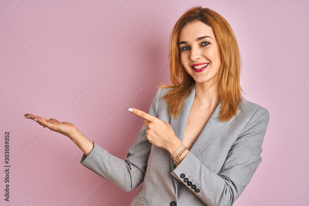 Young caucasian business woman wearing a suit over isolated pink background amazed and smiling to the camera while presenting with hand and pointing with finger. Young caucasian business woman wearing a suit over isolated pink background amazed and smiling to the camera while presenting with hand and pointing with finger.