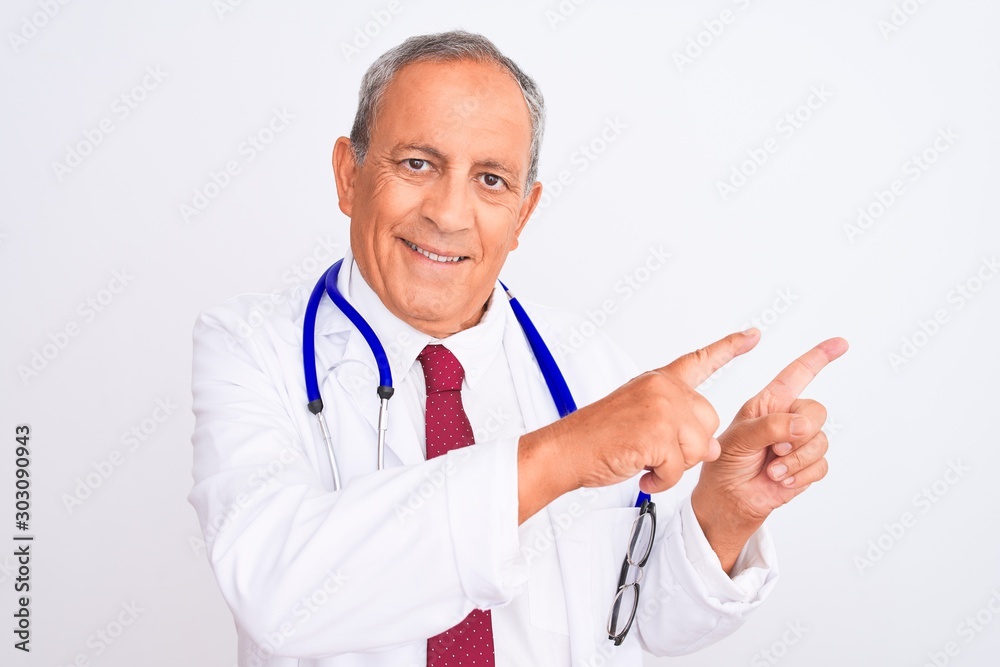 Senior grey-haired doctor man wearing stethoscope standing over isolated white background smiling and looking at the camera pointing with two hands and fingers to the side. Senior grey-haired doctor man wearing stethoscope standing over isolated white background smiling and looking at the camera pointing with two hands and fingers to the side.