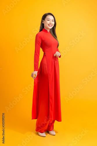 Elegant Asian woman standing over yellow background while wearing Vietnam tradion Ao dai custom. photo