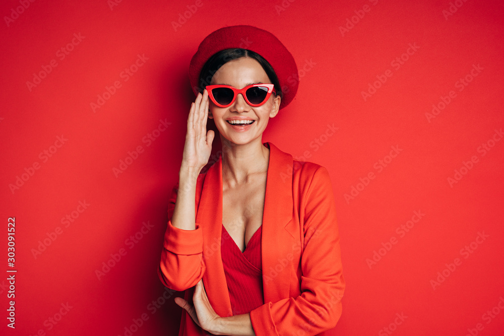 Positive, happy and cheerful young model posing on camera. Wear stylish fashionable red clothes. Look straight through sunglasses and smile. Fashio icon. Modern model .Isolated ovver red background. Positive, happy and cheerful young model posing on camera. Wear stylish fashionable red clothes. Look straight through sunglasses and smile. Fashio icon. Modern model .Isolated ovver red background.