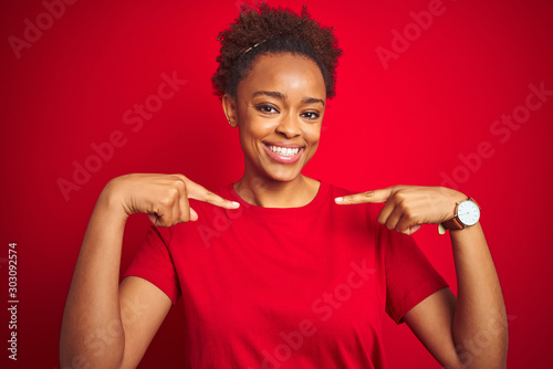 Young beautiful african american woman with afro hair over isolated red background looking confident with smile on face, pointing oneself with fingers proud and happy.