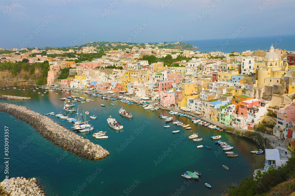 Panoramic view of beautiful Procida in sunny summer day. Colorful houses, cafes and restaurants, fishing boats and yachts in Marina Corricella, Procida Island, Italy.
