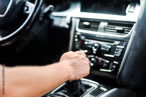 Man using gear on car manual gearbox for driving close up. Vehicle dashboard in background blured. Shifting the gear stick detail.