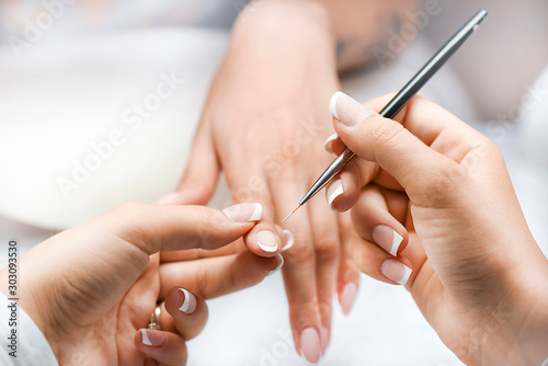Woman nails manicure close up. Nail profi paint white color or french with thin brush and pink background.