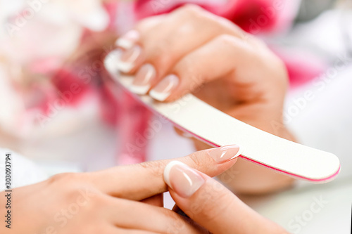 Beautician in salon applying nails art modelation. Manicure nail file in action  woman fingers on pink background.