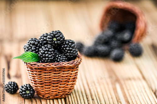 Blackberries in wooden wicker basket. Fresh juicy forest fruits like a blackberry with leaf on rustic table.