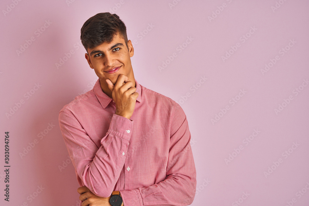 Young indian man wearing elegant shirt standing over isolated pink background looking confident at the camera smiling with crossed arms and hand raised on chin. Thinking positive. Young indian man wearing elegant shirt standing over isolated pink background looking confident at the camera smiling with crossed arms and hand raised on chin. Thinking positive.