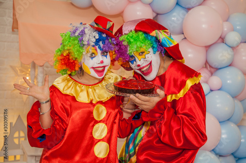 Fototapeta Naklejka Na Ścianę i Meble -  Funny clowns from the circus. Clown boy and clown girl holding a cake in their hands. The emotions of the holiday.