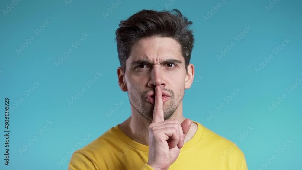 European handsome man holding finger on his lips over blue background. Gesture of shhh, secret, silence. European handsome man holding finger on his lips over blue background. Gesture of shhh, secret, silence.
