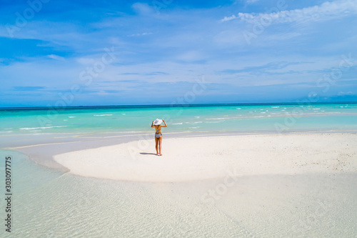 Summer holiday fashion concept - tanning girl wearing sun hat at the beach on a white sand shot from above.Top view from drone. Aerial view of slim woman sunbathing lying on a beach in Maldives.