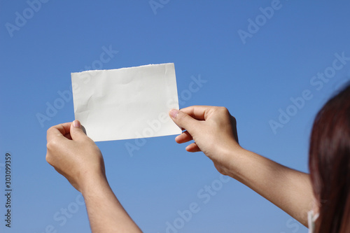 Hand hold white blank paper on blue sky background.