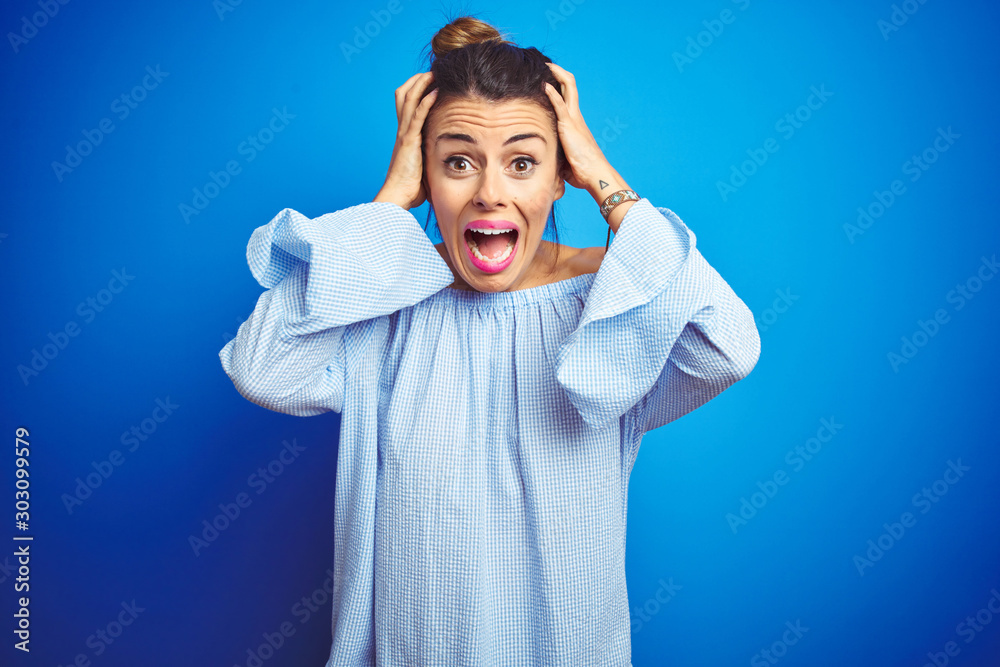 Young beautiful woman wearing bun hairstyle over blue isolated background Crazy and scared with hands on head, afraid and surprised of shock with open mouth Young beautiful woman wearing bun hairstyle over blue isolated background Crazy and scared with hands on head, afraid and surprised of shock with open mouth