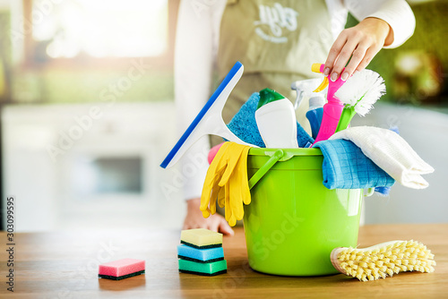 Cleaning items on floor in modern kitchen. Woman maid or charwoman blured in background. Bucket, brush, washcloth, spray.