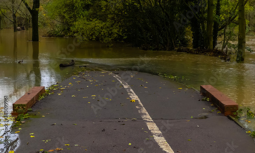 A public footpath blocked by floodwater from a river that has burst its banks following heavy Autumnal rain. White centre line disappearing under water. Landscape image with space for copy. England. photo