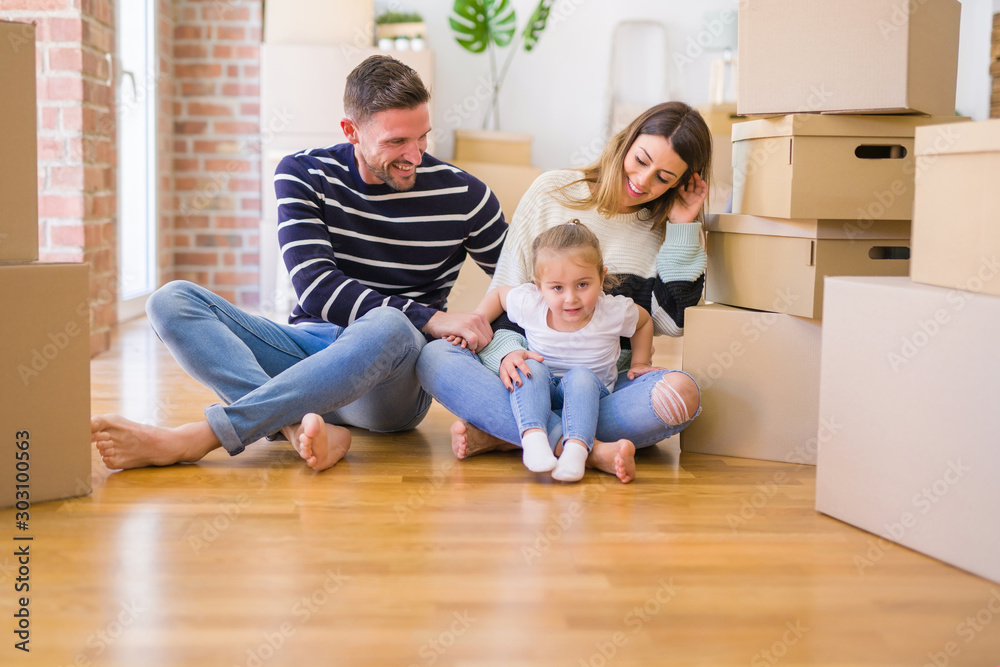 Beautiful family sitting on the floor playing with his kid at new home around cardboard boxes