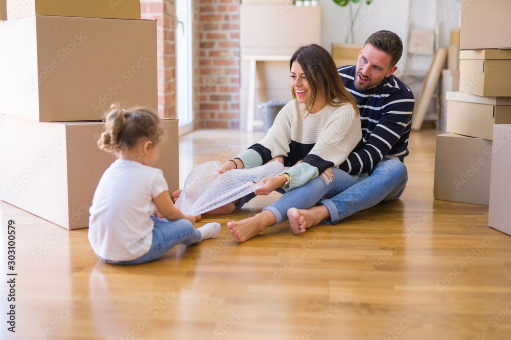 Beautiful family sitting on the floor playing with his kid at new home around cardboard boxes Beautiful family sitting on the floor playing with his kid at new home around cardboard boxes