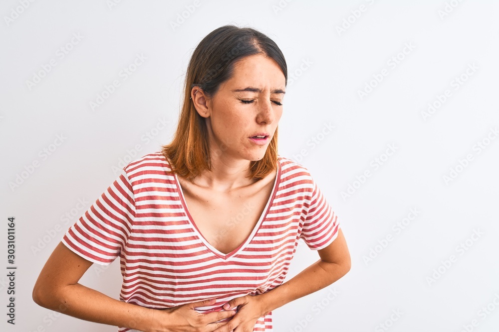 Beautiful redhead woman wearing casual striped red t-shirt over isolated background with hand on stomach because indigestion, painful illness feeling unwell. Ache concept. Beautiful redhead woman wearing casual striped red t-shirt over isolated background with hand on stomach because indigestion, painful illness feeling unwell. Ache concept.