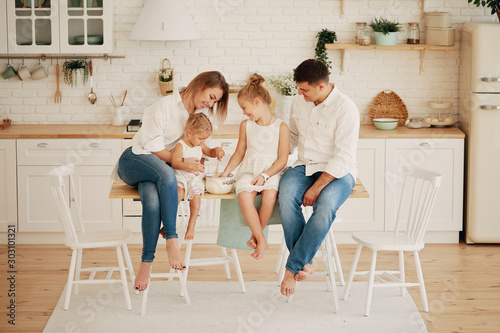 Happy smiling caucasian family in the kitchen preparing breakfast. Parents with two young children are sitting at the dining table and having fun. Family values