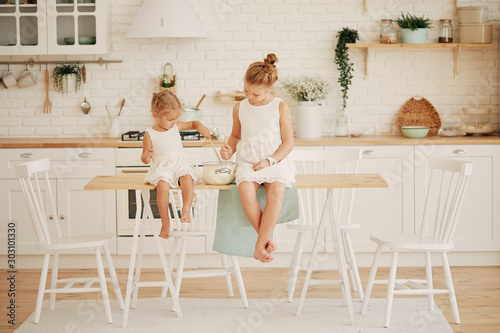 Two little girls sisters are sitting at the dining table in the kitchen. The concept of home comfort. Modern repair in the house © oes