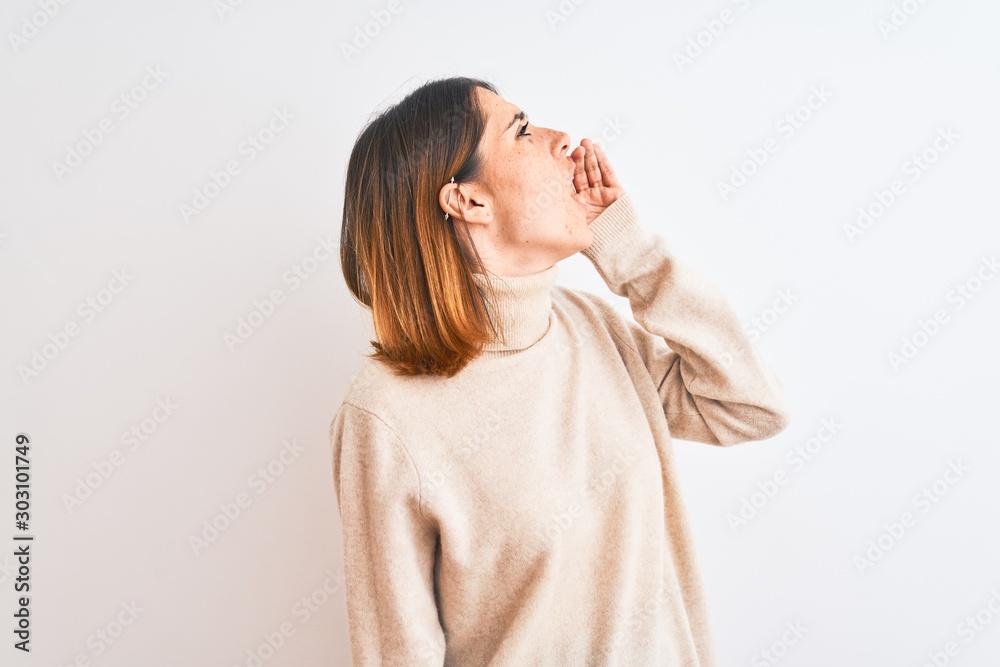 Beautiful redhead woman wearing winter turtleneck sweater over isolated background shouting and screaming loud to side with hand on mouth. Communication concept. Beautiful redhead woman wearing winter turtleneck sweater over isolated background shouting and screaming loud to side with hand on mouth. Communication concept.