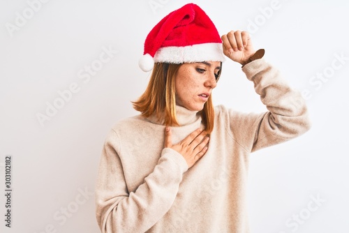 Beautiful redhead woman wearing christmas hat over isolated background Touching forehead for illness and fever, flu and cold, virus sick