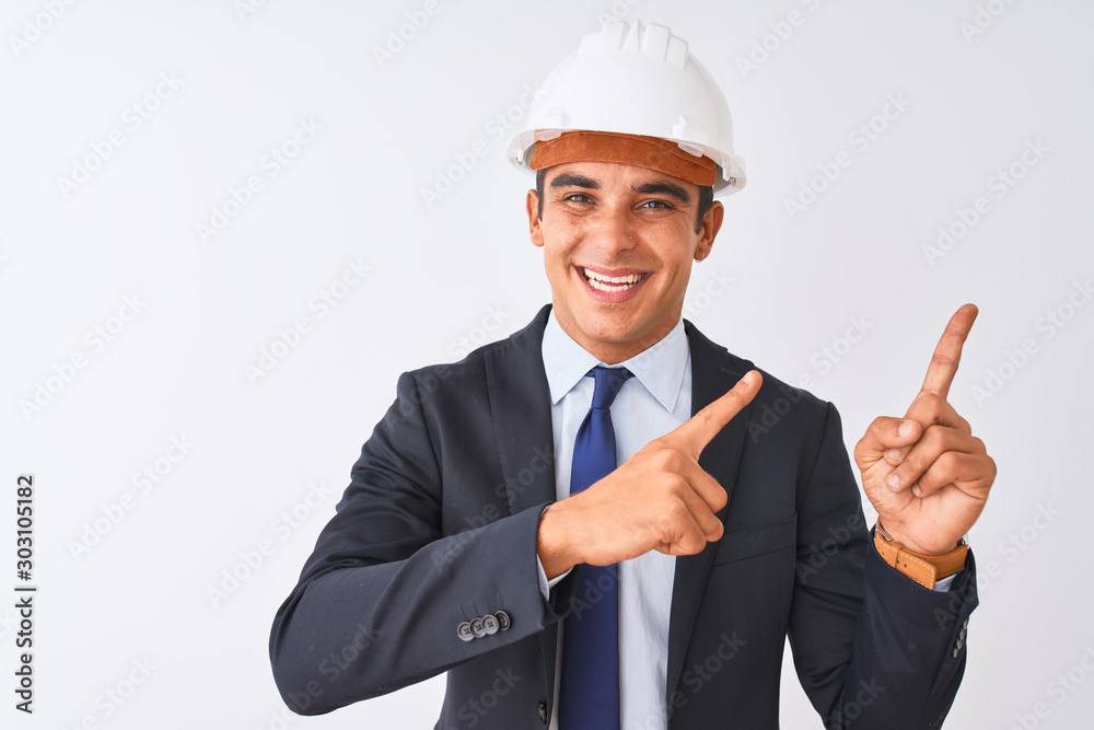 Young handsome architect man wearing suit and helmet over isolated white background smiling and looking at the camera pointing with two hands and fingers to the side.