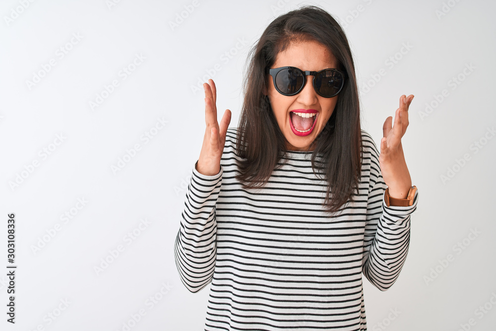 Chinese woman wearing striped t-shirt and sunglasses standing over isolated white background celebrating mad and crazy for success with arms raised and closed eyes screaming excited. Winner concept Chinese woman wearing striped t-shirt and sunglasses standing over isolated white background celebrating mad and crazy for success with arms raised and closed eyes screaming excited. Winner concept