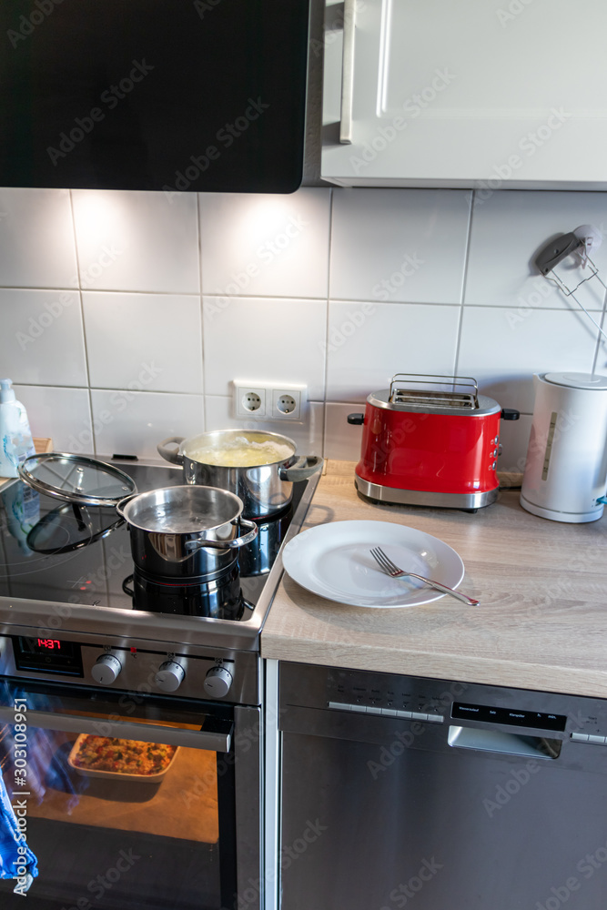 Hausfrau kocht Nudeln und Wasser für das Mittagessen mit der Familie in silbernen Töpfen auf Induktionsherd mit heißen Kochfeldern als leckeres Mahl Hausfrau kocht Nudeln und Wasser für das Mittagessen mit der Familie in silbernen Töpfen auf Induktionsherd mit heißen Kochfeldern als leckeres Mahl