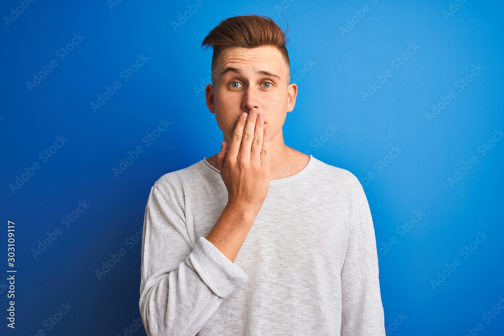Young handsome man wearing white casual t-shirt standing over isolated blue background cover mouth with hand shocked with shame for mistake, expression of fear, scared in silence, secret concept Young handsome man wearing white casual t-shirt standing over isolated blue background cover mouth with hand shocked with shame for mistake, expression of fear, scared in silence, secret concept
