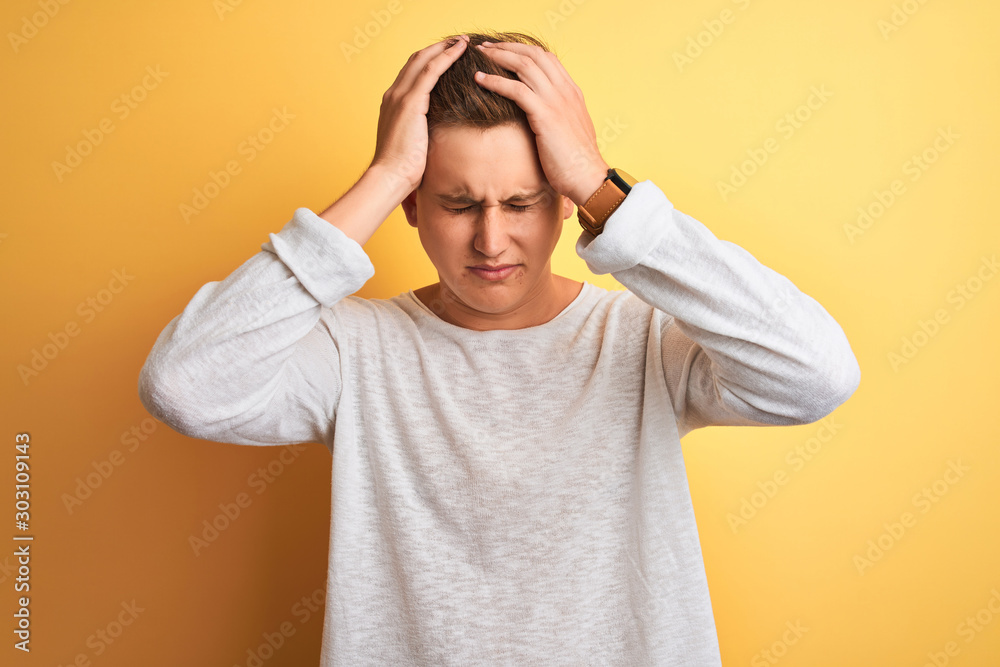 Young handsome man wearing white casual t-shirt standing over isolated yellow background suffering from headache desperate and stressed because pain and migraine. Hands on head. Young handsome man wearing white casual t-shirt standing over isolated yellow background suffering from headache desperate and stressed because pain and migraine. Hands on head.