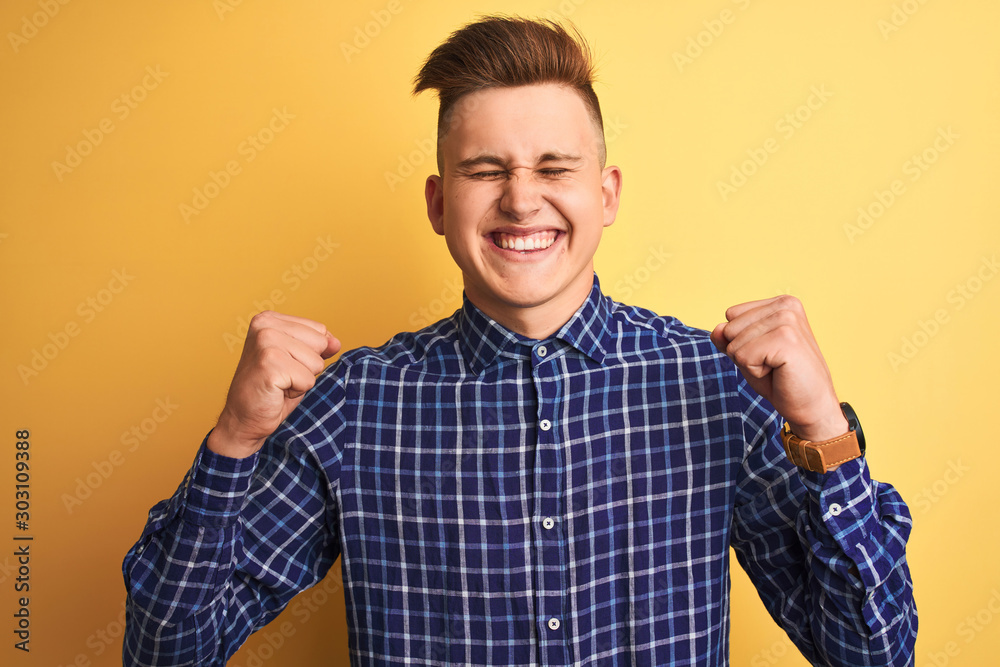 Young handsome man wearing casual shirt standing over isolated yellow background excited for success with arms raised and eyes closed celebrating victory smiling. Winner concept. Young handsome man wearing casual shirt standing over isolated yellow background excited for success with arms raised and eyes closed celebrating victory smiling. Winner concept.