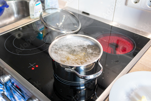 Hausfrau kocht Nudeln und Wasser für das Mittagessen mit der Familie in silbernen Töpfen auf Induktionsherd mit heißen Kochfeldern als leckeres Mahl