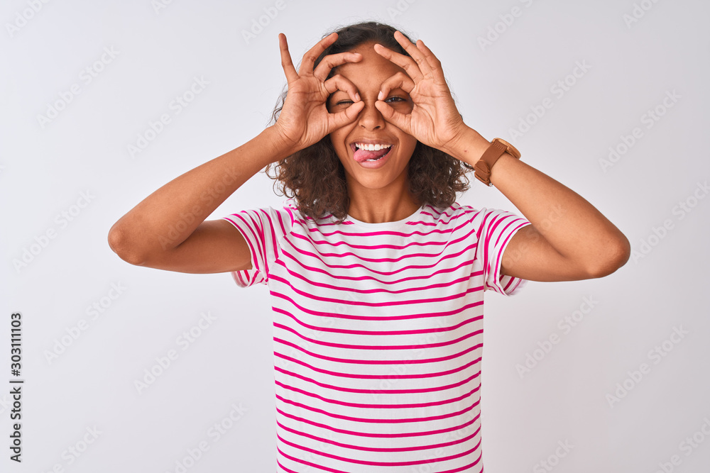 Young brazilian woman wearing pink striped t-shirt standing over isolated white background doing ok gesture like binoculars sticking tongue out, eyes looking through fingers. Crazy expression. Young brazilian woman wearing pink striped t-shirt standing over isolated white background doing ok gesture like binoculars sticking tongue out, eyes looking through fingers. Crazy expression.