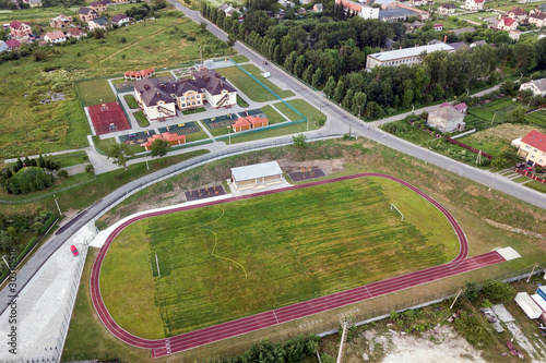 Aerial view of a football field on a stadium covered with green grass in rural town area.