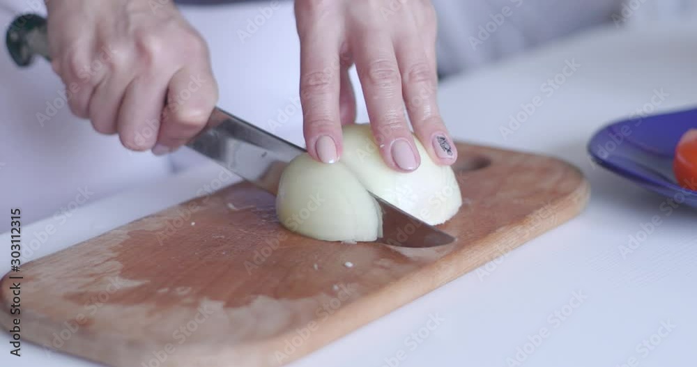 Onion on the cut board. Woman`s hands with a knife slices onion on the cut board. Onion on the table.