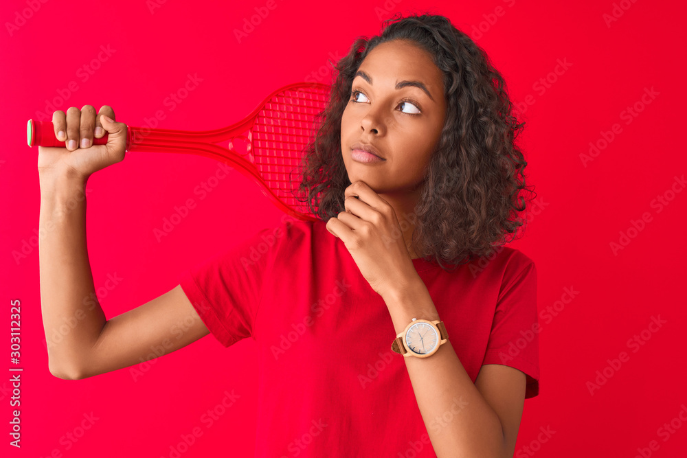 Naklejka premium Young brazilian sportswoman holding tennis racket standing over isolated red background serious face thinking about question, very confused idea