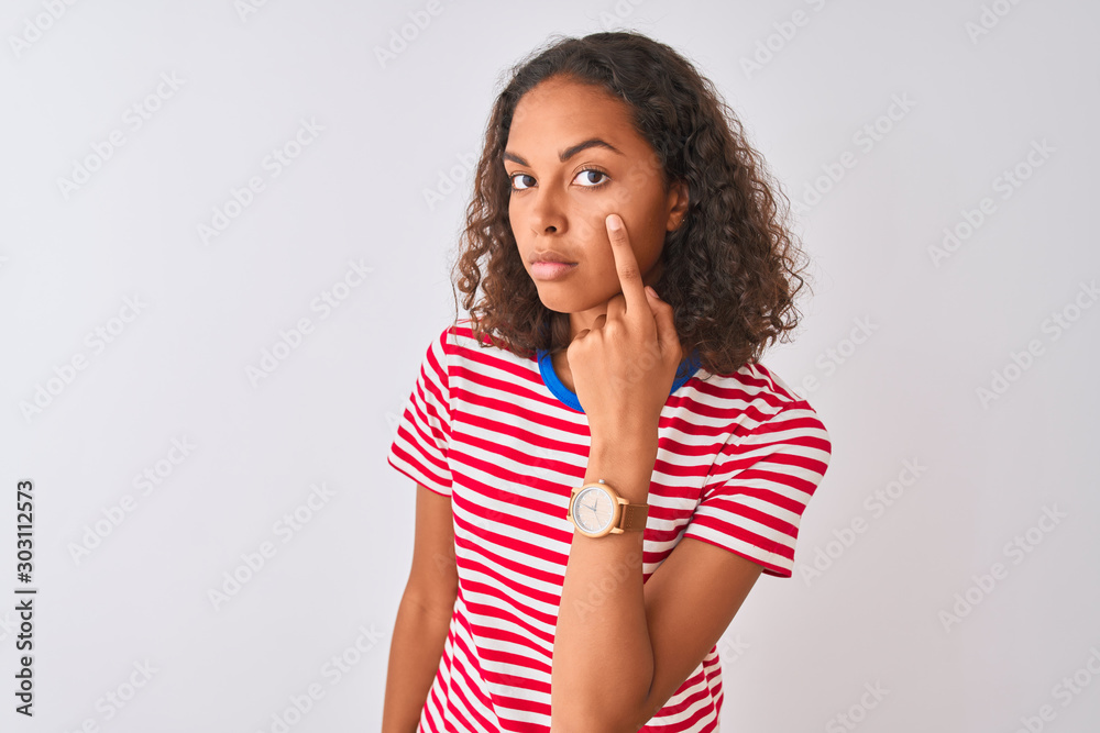Young brazilian woman wearing red striped t-shirt standing over isolated white background Pointing to the eye watching you gesture, suspicious expression Young brazilian woman wearing red striped t-shirt standing over isolated white background Pointing to the eye watching you gesture, suspicious expression