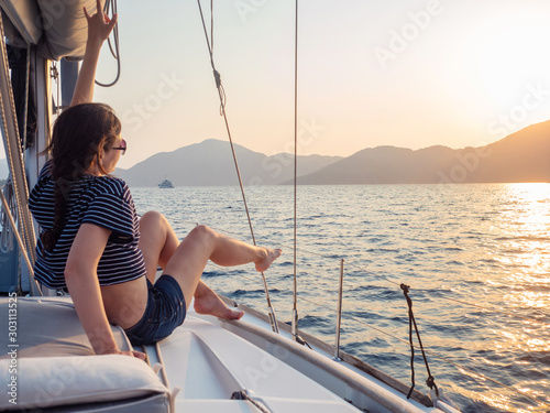 attractive young woman in a striped t-shirt enjoys the sunset on the deck of a sailing yacht. Sailing regatta