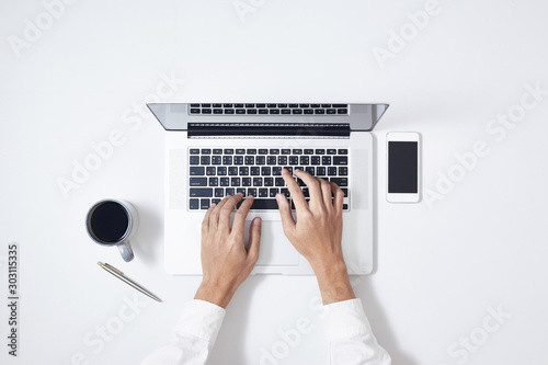A man is typing on laptop keyboard on modern white office desk, top view. photo