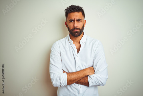 Young indian man wearing elegant shirt standing over isolated white background skeptic and nervous, disapproving expression on face with crossed arms. Negative person.