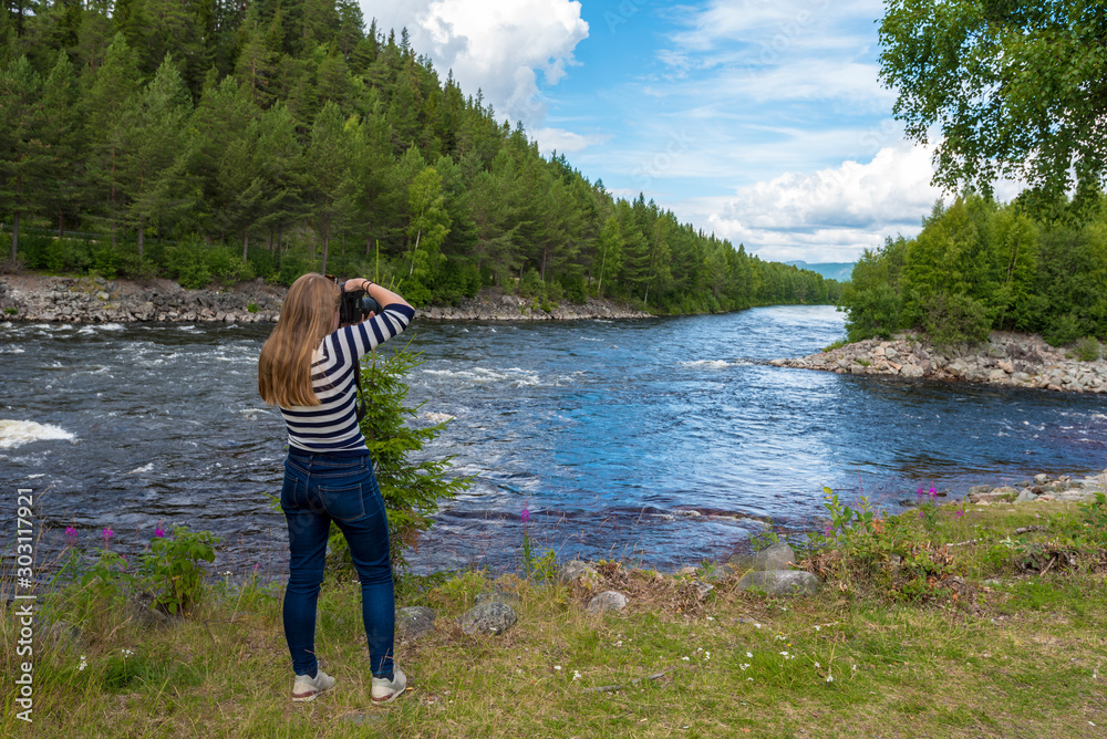 Young woman is photographing the landscape in the border of Fugga river in Hedmark county of Norway.
